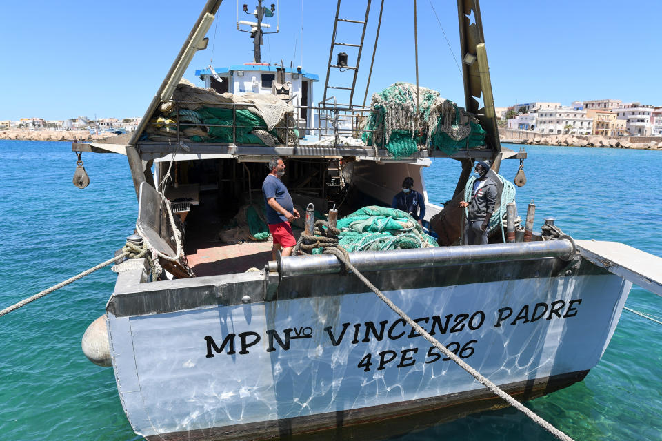 Waly Sarr, 30, right, and Ibrahima Mbaye, 41, center, both from Senegal, and Salvatore Di Battista fix nets on the deck of the "Vincenzo Padre" fishing boat where they work as fishermen, in the Island of Lampedusa, southern Italy, Thursday, May 13, 2021. The tiny island of Lampedusa, which is closer to Africa than the Italian mainland, is in the throes of yet another season of migrant arrivals, and Mbaye and Sarr can only watch from shore as their fellow African countrymen risk their lives to get here via smugglers' boats. (AP Photo/Salvatore Cavalli)