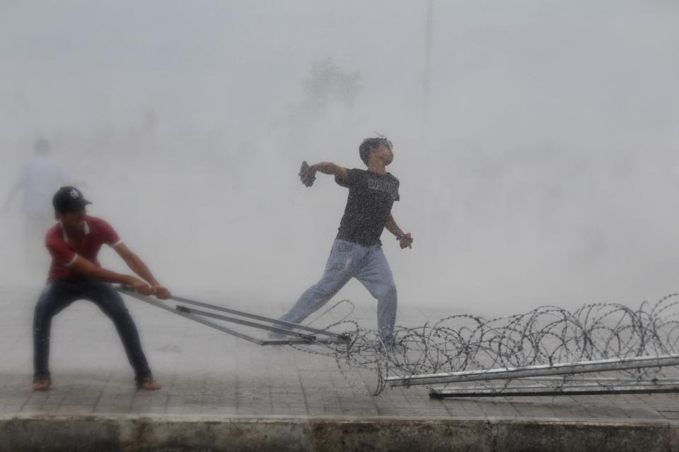 A protester supporting the opposition Cambodia National Rescue Party (CNRP) throws a stone as another tries to remove barbed wire barricades during clashes with police officers near the Royal Palace in central Phnom Penh September 15, 2013. (REUTERS/Samrang Pring)