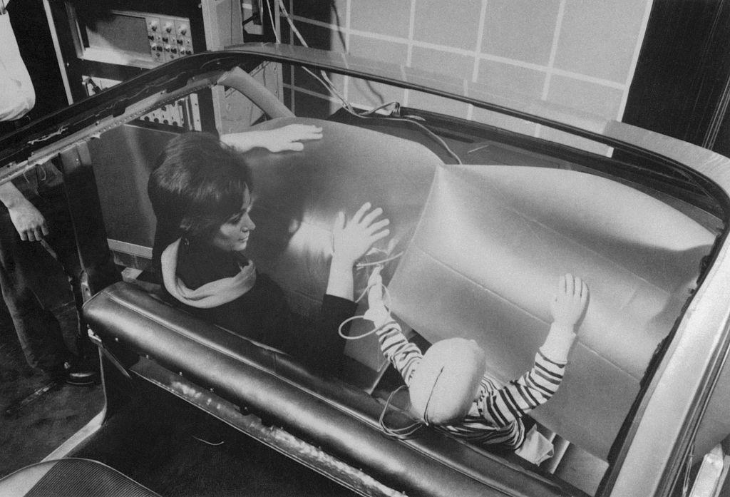 girl and a dummy of a child serve as the subjects in this demonstration of a new auto crash restraint system, 1968