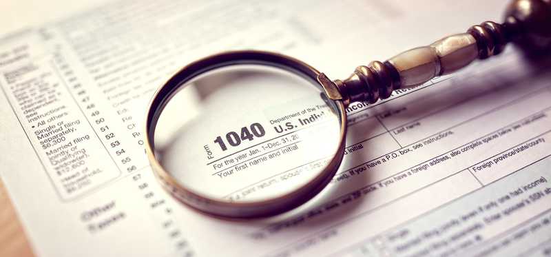 A magnifying glass sits on top of a 1040 tax form.