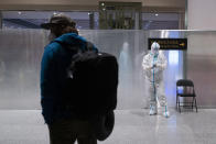 FILE - A passenger waits in the holding area in front of a member of airport personnel wearing protective gear at the Beijing Capital International Airport ahead of the 2022 Winter Olympics in Beijing, Jan. 24, 2022. (AP Photo/Jae C. Hong, File)