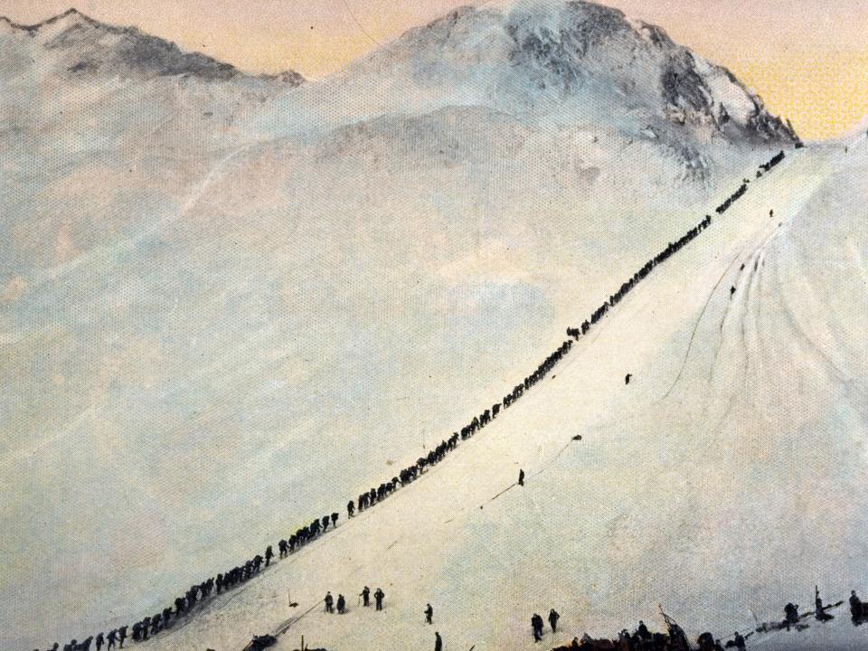 Long line of gold prospectors climb the stairs cut into the ice on the Chilkoot Trail through Chilkoot Pass during the Klondike Gold Rush. The temporary tent settlement called The Scales sits on a flat below the stairs, 1896.