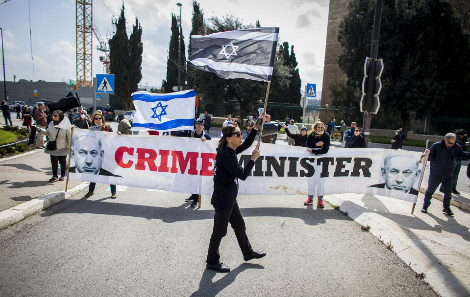 People wave Israeli flags during a protest outside the Israeli parliament in Jerusalem, Thursday, March 19, 2020. Hundreds of people defied restrictions on large gatherings to protest outside parliament Thursday, while scores of others were blocked by police from reaching the area as they accused Prime Minister Benjamin Netanyahu's government of exploiting the coronavirus crisis to solidify his power and undermine Israel's democratic foundations. (AP Photo/Eyal Warshavsky)