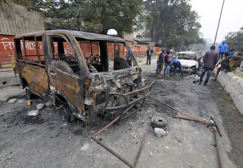People stand next to vehicles that were set ablaze by demonstrators during a protest on Thursday, after India's parliament passed a Citizenship Amendment Bill, in Guwahati