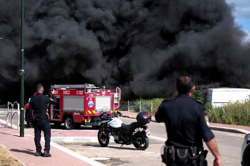 Israeli policemen stand next to smoke from a fire following incoming rockets from Lebanon to Israel in Bezet, northern Israel