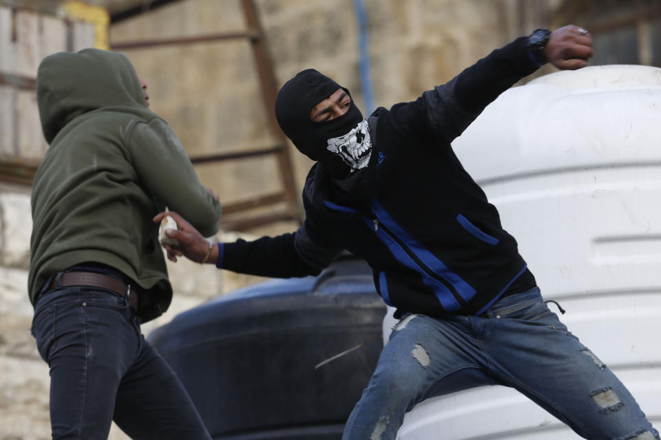 Palestinian protesters hurl stones towards Israeli soldiers during clashes in the West Bank city of Hebron, Thursday, Feb. 6, 2020. Israeli forces have killed two Palestinians in clashes in the occupied West Bank and a third in Jerusalem after he opened fire at a police officer. The killings came hours after a car-ramming attack elsewhere in the city Thursday wounded 12 Israeli soldiers. Tensions have soared following last week's release of President Donald Trump's Mideast initiative, which greatly favors Israel and was rejected by the Palestinians. (AP Photo/Majdi Mohammed)