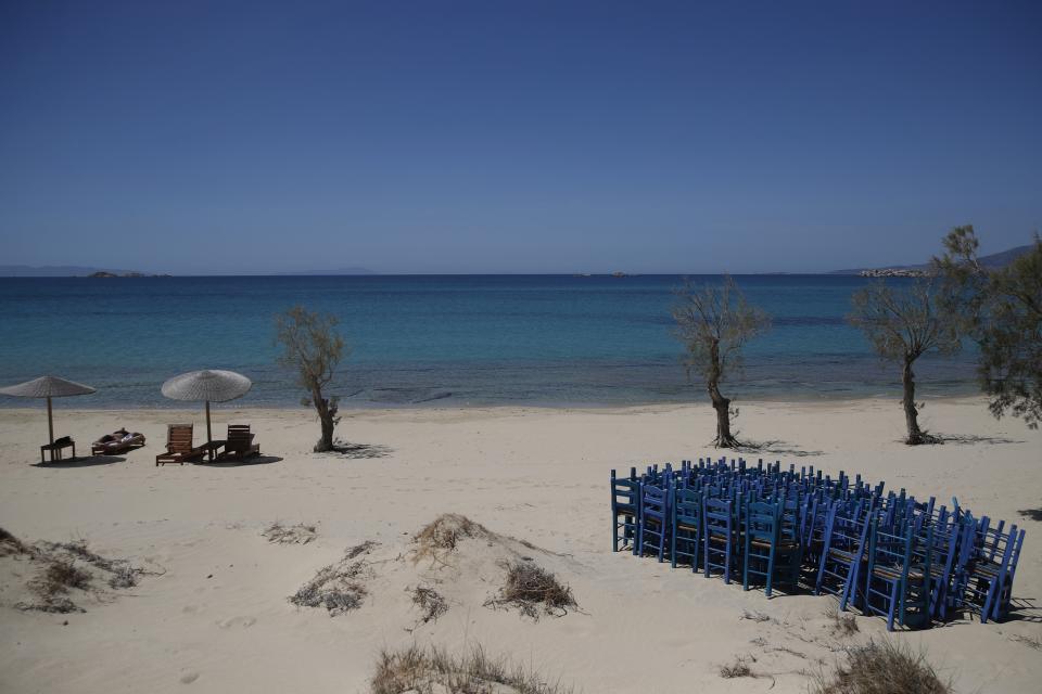 A tourist enjoys the sun as tavern chairs are stored at Plaka beach on the Aegean island of Naxos, Greece, Wednesday, May 12, 2021. With debts piling up, southern European countries are racing to reopen their tourism services despite delays in rolling out a planned EU-wide travel pass. Greece Friday became the latest country to open up its vacation season as it dismantles lockdown restrictions and focuses its vaccination program on the islands. (AP Photo/Thanassis Stavrakis)