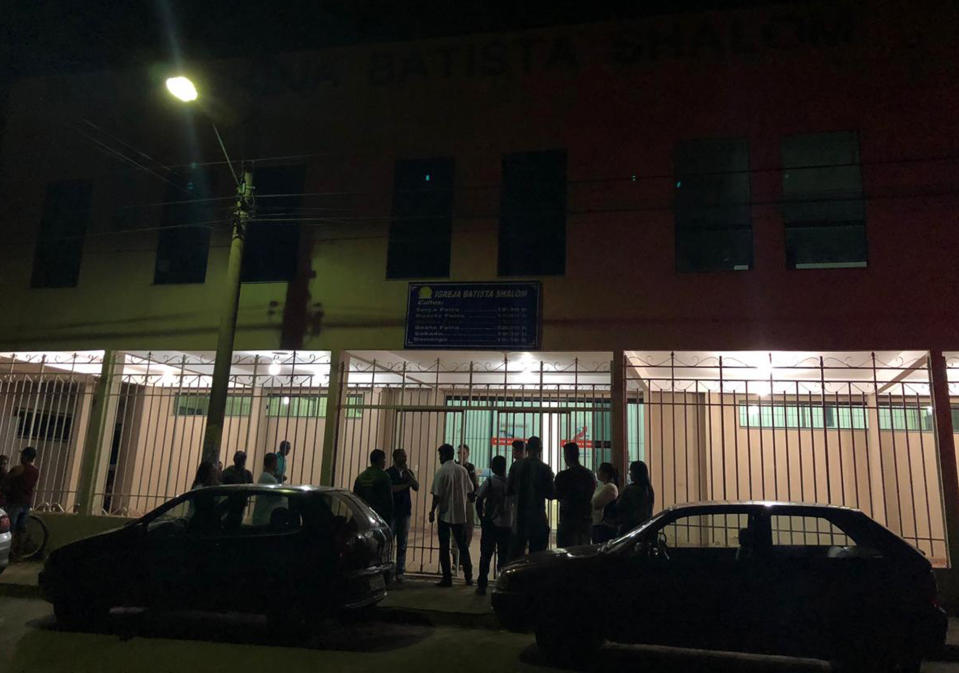 En esta foto publicada por Agora News, los residentes se ubican en la entrada de una iglesia bautista donde un hombre mató a tres personas después de asesinar a su exnovia en Paracatu, estado de Minas Gerais, Brasil, el martes 21 de mayo de 2019. (Marco Aurelio Costa / Agora News vía AP)