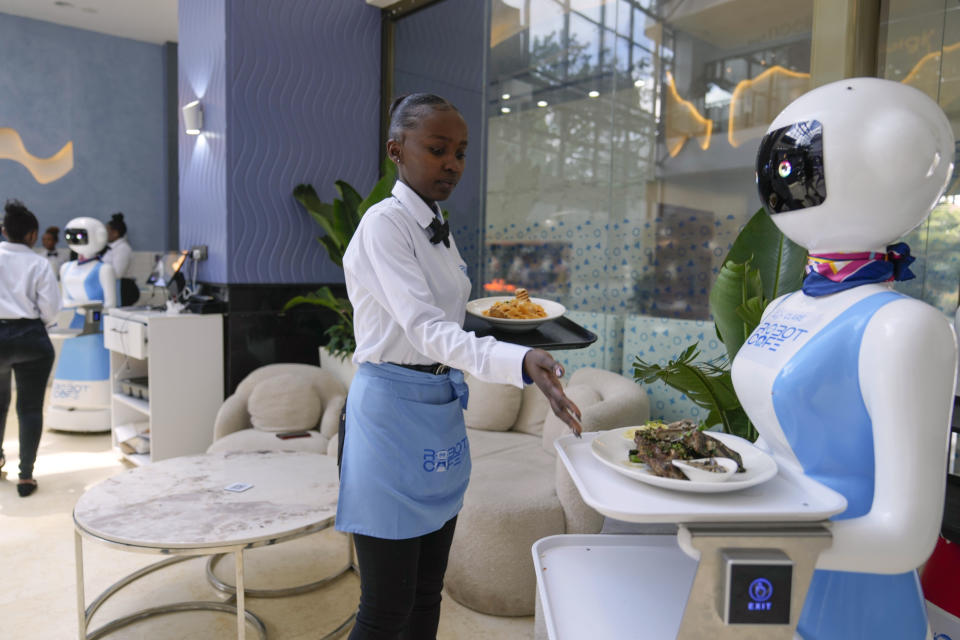 Robotic waiter Claire, receives an order from a human waiter to deliver to customers at the Robot Cafe in Nairobi, Kenya Thursday, Aug. 29, 2024. The three robots, christened Claire, R24 and Nadia, are not programmed to have a full conversation with customers, but they can say "Your order is ready, Welcome" then people have to press an exit button after picking up their food from the tray. (AP Photo/Brian Inganga)