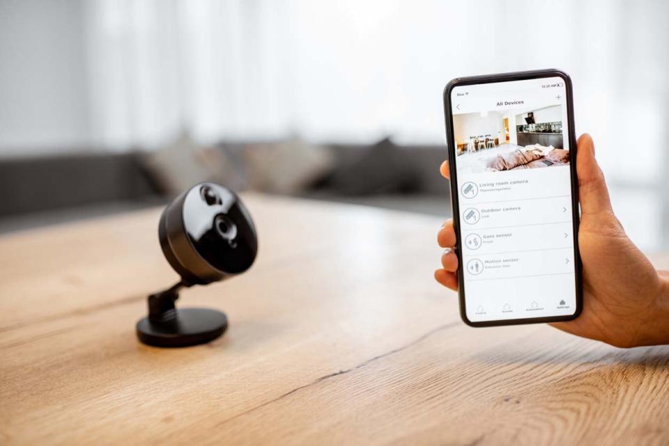 A close up of a home security camera on a table next to a smart phone screen showing the feed. 