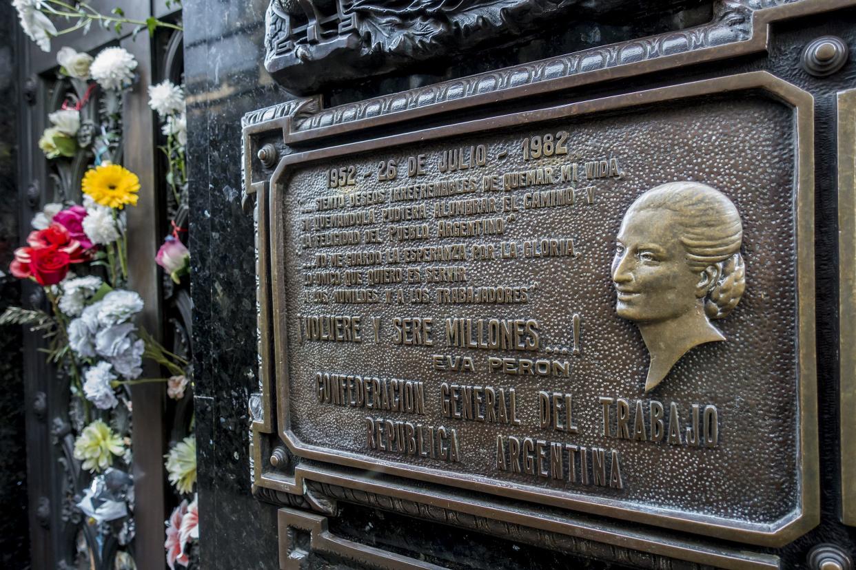 Closeup of headstone of Eva Perón's grave in La Recoleta Cemetery, Buenos Aires, Argentina with several colorful flowers through the lattice on the left