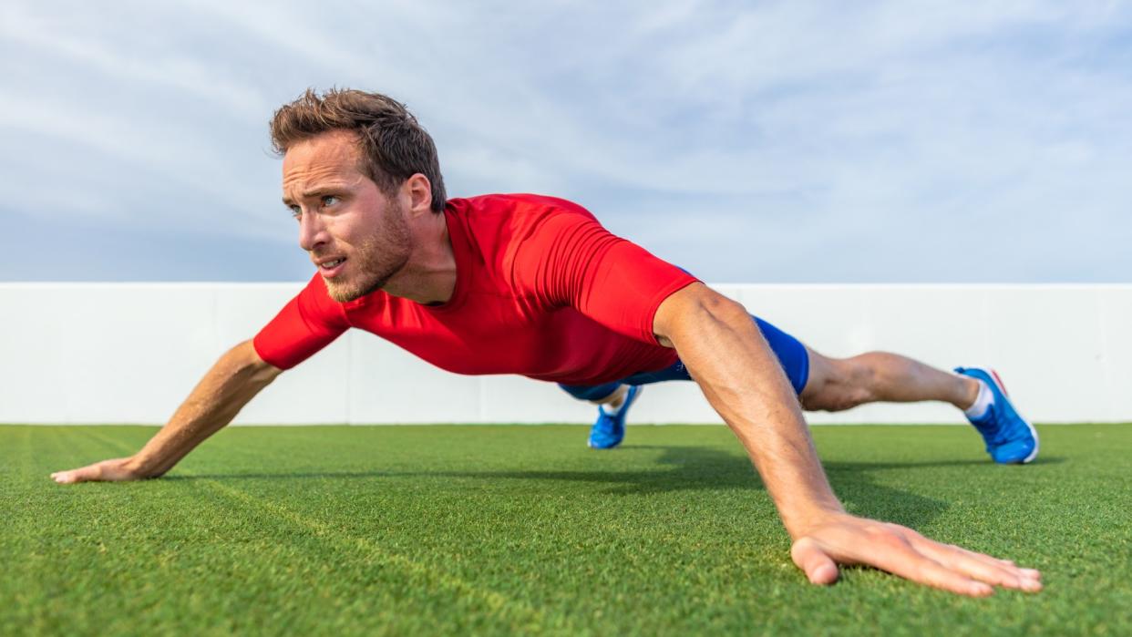  Man outdoors on grass performing an X plank with arms and feet wide. 