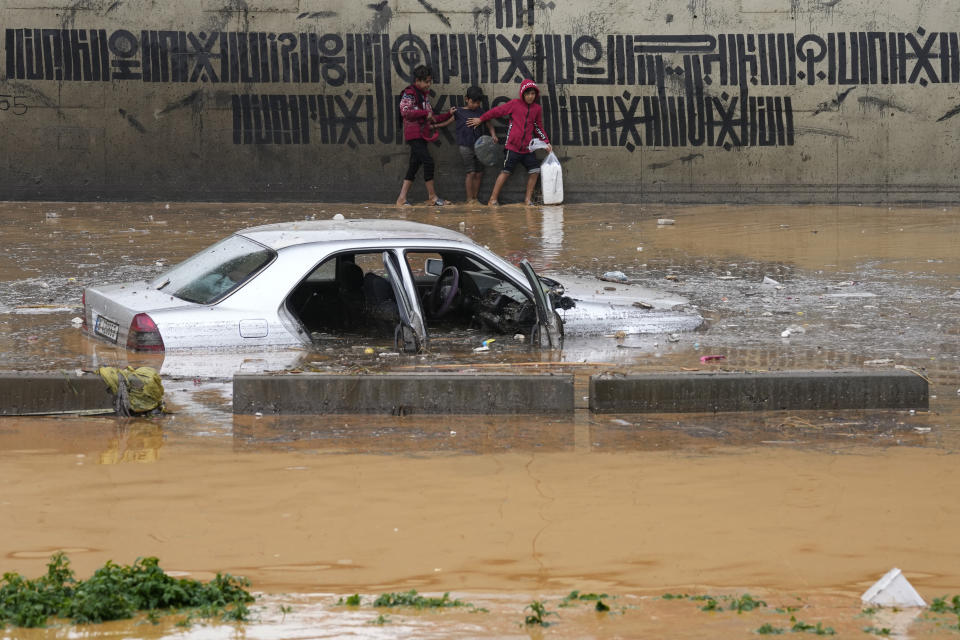 Street vendor boys pass in front of a car submerged in flood water at a highway that flooded by the rains, in Beirut, Lebanon, Saturday, Dec. 23, 2023. A rainstorm has paralysed parts of Lebanon's cities, turning streets to small rivers, stranding motorists inside their vehicles and damaging homes in some areas. (AP Photo/Hussein Malla)