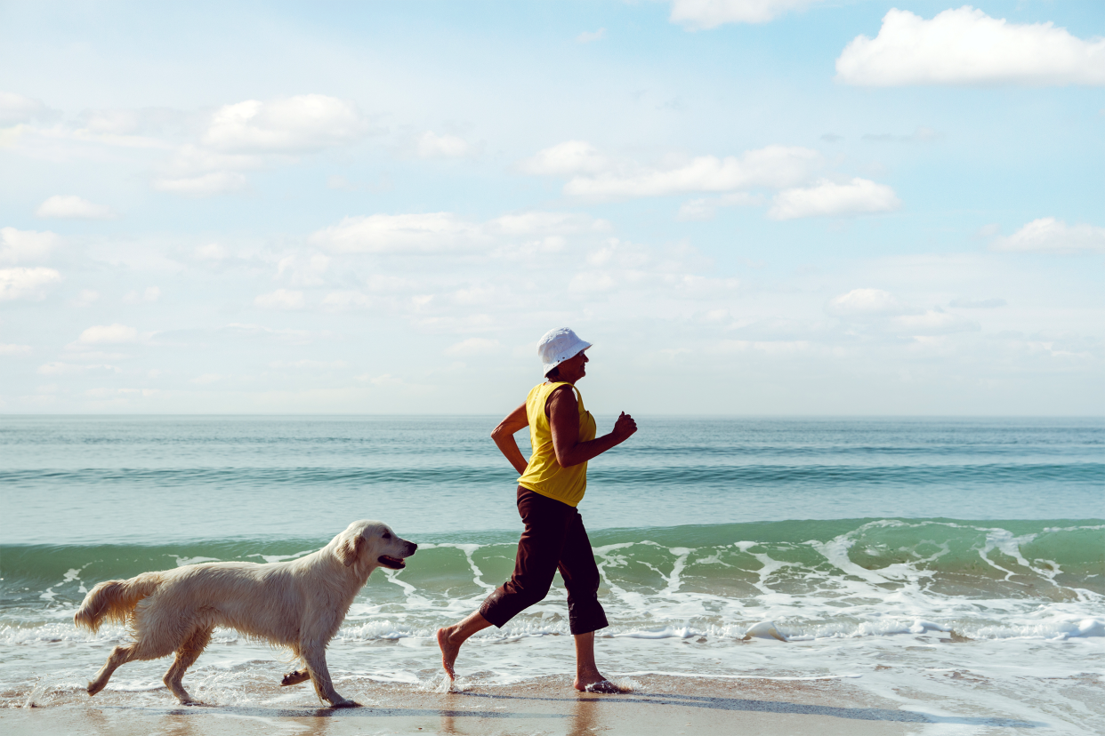 senior woman running with dog on beach
