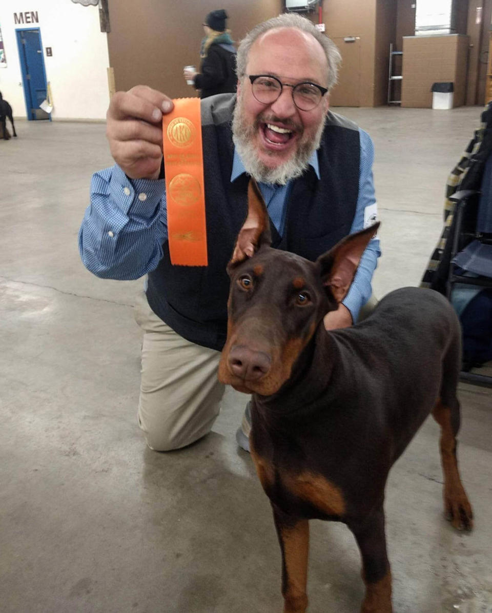 Paul Peavey sostiene un premio mientras se arrodilla detrás de un dóberman (Elite European Dobermans)