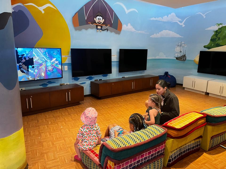 Kid's Club with blue walls painted to look like a sea with a ship and a monkey decoration. An adult and three children watch TV