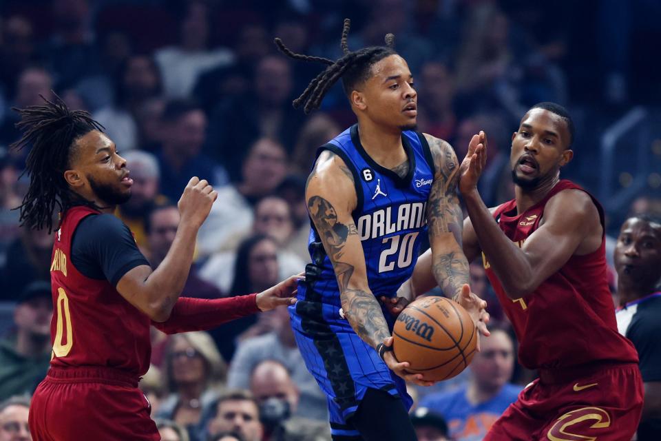 Orlando Magic guard Markelle Fultz (20) passes the ball from between Cleveland Cavaliers forward Evan Mobley (4) and guard Darius Garland (10) during the first half of an NBA basketball game Friday, Dec. 2, 2022, in Cleveland. (AP Photo/Ron Schwane)