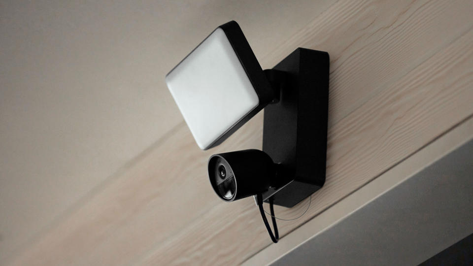 Philips Hue Secure floodlight camera in black attached to a wood wall possibly above a garage door