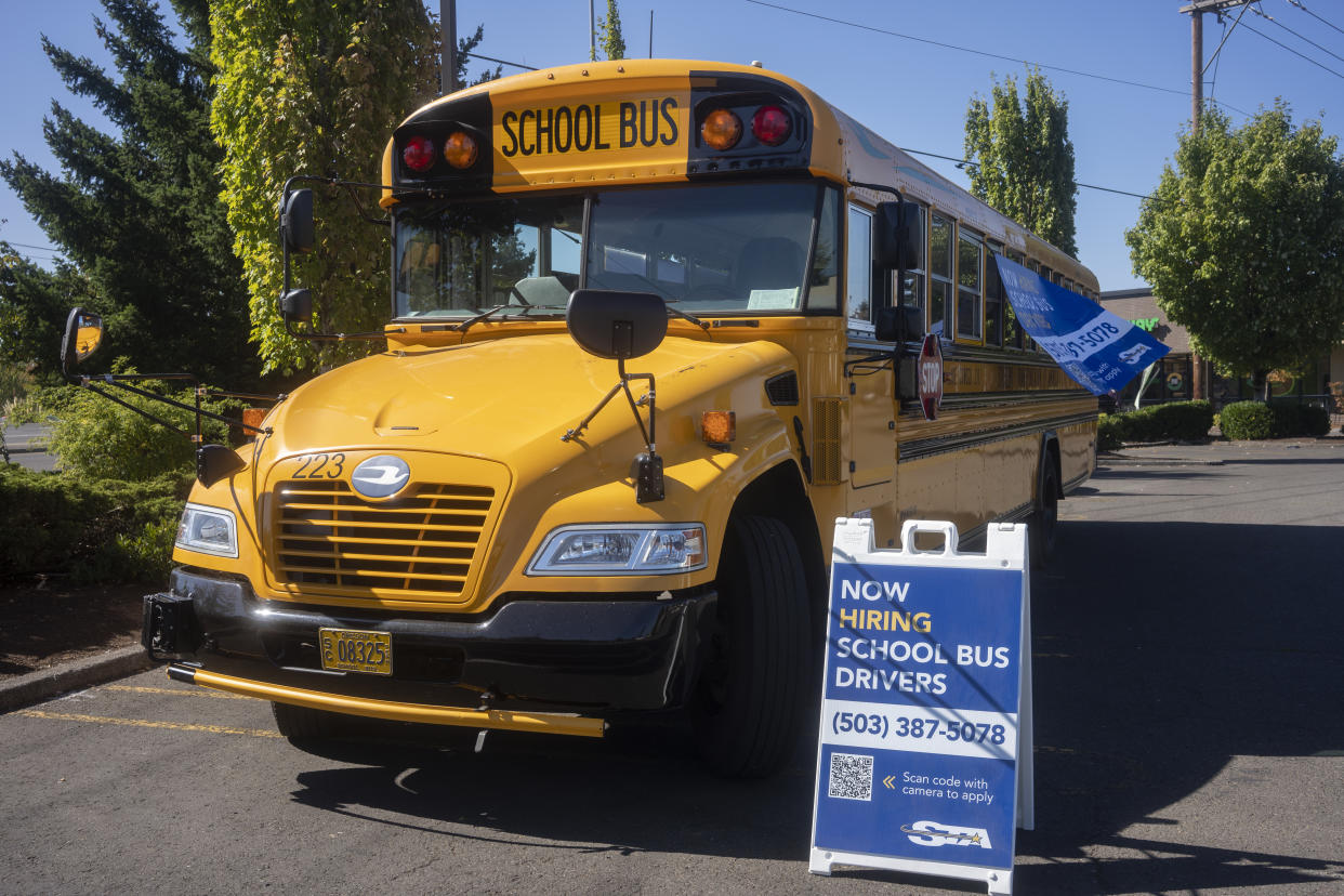 Lake Oswego, OR, USA - Sep 8, 2021: Now Hiring School Bus Drivers sign is seen next to an empty school bus operated by STA (Student Transportation of America) in Lake Oswego, Oregon.