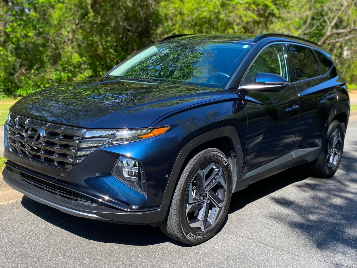 A dark blue Hyundai Tucson Hybrid SUV parked in front of green woods.