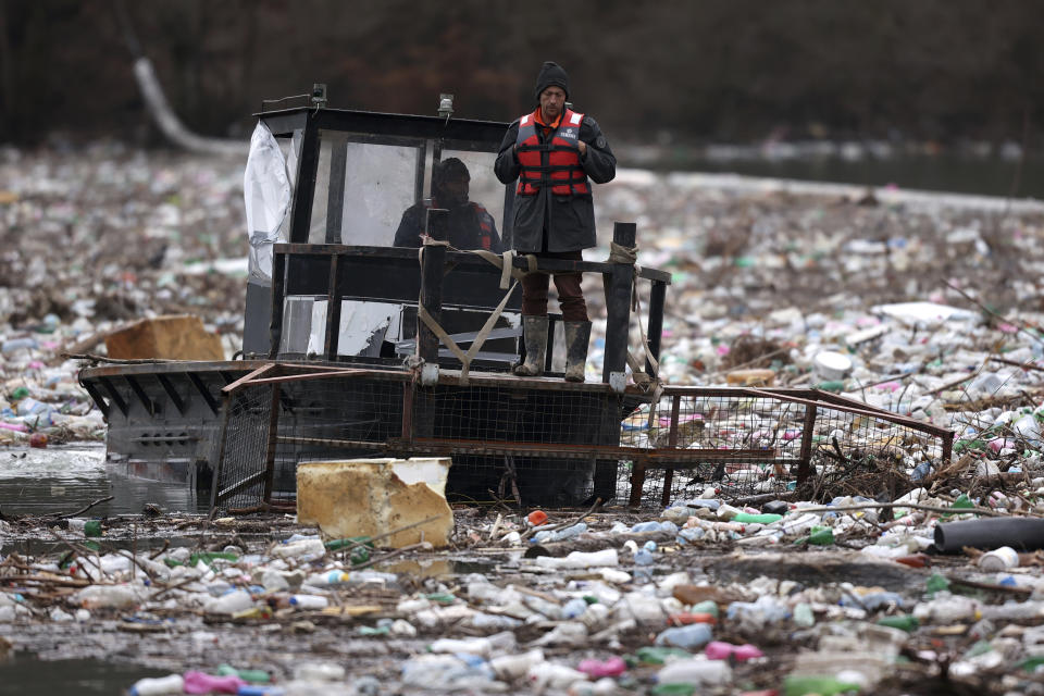 Utility company workers push the waste to the shore of Lim river near Priboj, Serbia, Monday, Jan. 30, 2023. Plastic bottles, wooden planks, rusty barrels and other garbage dumped in poorly regulated riverside landfills or directly into the rivers accumulated during high water season, behind a trash barrier in the Lim river in southwestern Serbia. (AP Photo/Armin Durgut)