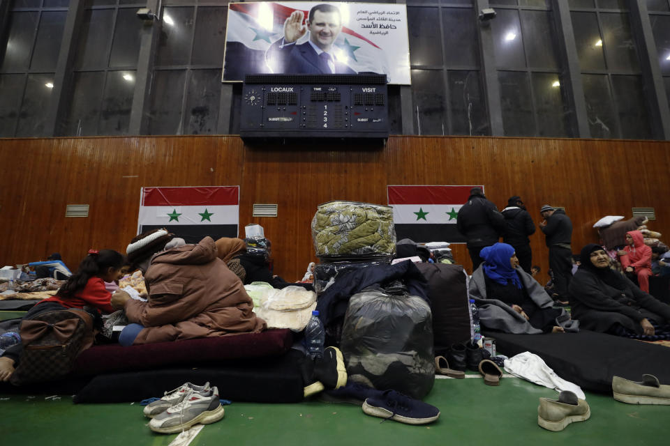 Displaced people sit inside a sports stadium following a devastating earthquake, in the coastal city of Latakia, Syria, Friday, Feb. 10, 2023. The 7.8 magnitude earthquake that hit Turkey and Syria, killing more than 23,000 this week has displaced millions of people in war-torn Syria. The country's 12-year-old uprising turned civil war had already displaced half the country's pre-war population of 23 million before the earthquake. A picture of Syrian President Bashar Assad hangs on the wall. (AP Photo/Omar Sanadiki)