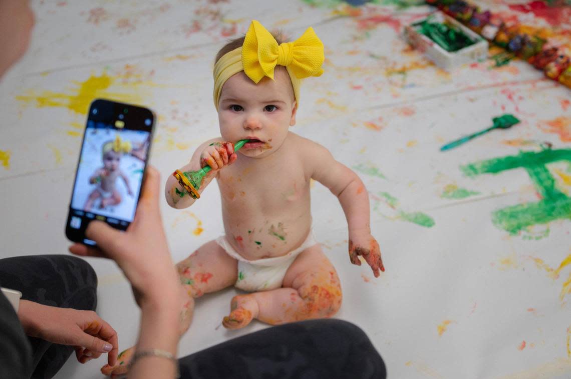 Eight-month-old Alice Sloderbeck chews on a paintbrush while having her photo taken during the baby paint crawl.