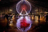 FILE - An illuminated Ferris wheel is reflected in the wet pavement at a Christmas fair which opened ahead of the holiday season in Bucharest, Romania, Nov. 20, 2022. In cities across Europe, officials are wrestling with a choice this Christmas. Dim lighting plans to send a message of energy conservation and solidarity with citizens squeezed by both higher energy costs and inflation or let the lights blaze in a message of defiance after two years of pandemic-suppressed Christmas seasons, creating a mood that retailers hope loosen holiday purses. (AP Photo/Andreea Alexandru, File)