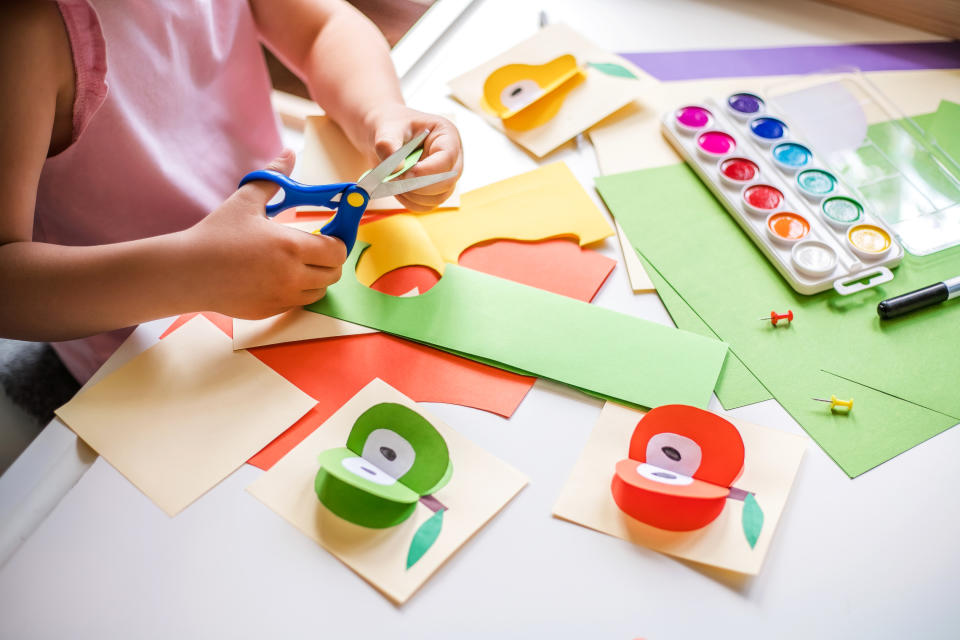 Little girl cutting colorful paper at the table at home.