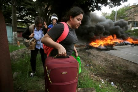 People walk past a burning barricade set by demonstrators during a protest against President Juan Orlando Hernandez government's plans to privatize healthcare and education, in Tegucigalpa