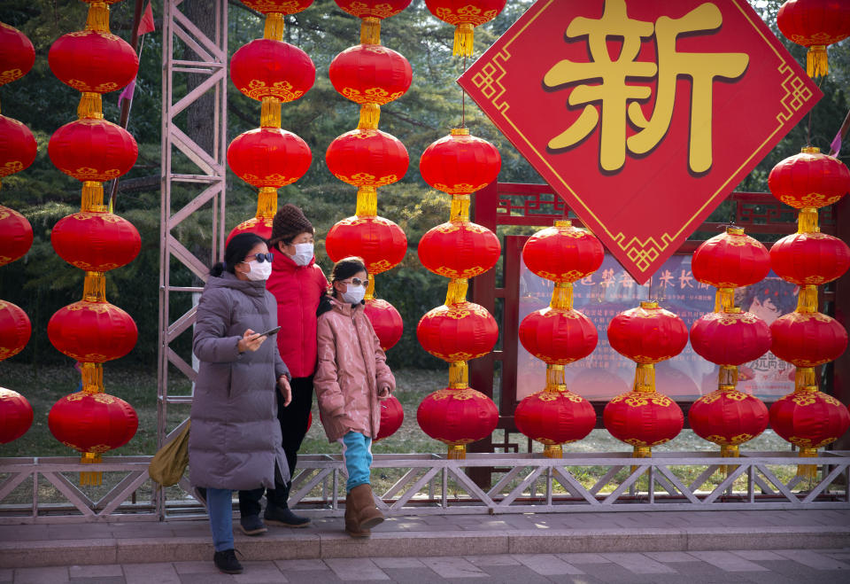 Personas con máscaras médicas posan para la foto frente a decoraciones de una feria de un templo cancelada con motivo del Año Nuevo Lunar en el Parque Longtan, en Beijing, el sábado 25 de enero de 2020. (AP Foto/Mark Schiefelbein)