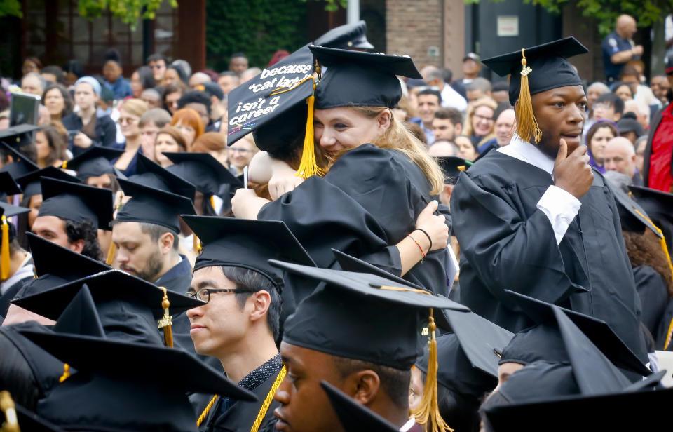 Andrew Dorilas, left, a music major from from Spring Valley, N.Y., walks past fellow music major graduates Charlotte Bennett, center, from Pawling, N.Y., and Isabel Saline, Queens, N.Y. as they hug during commencement for City College of New York (CCNY) division of Humanities and the Arts graduates, Wednesday May 31, 2017, in New York. Bennett, who sang the national anthem to start the ceremony, said 