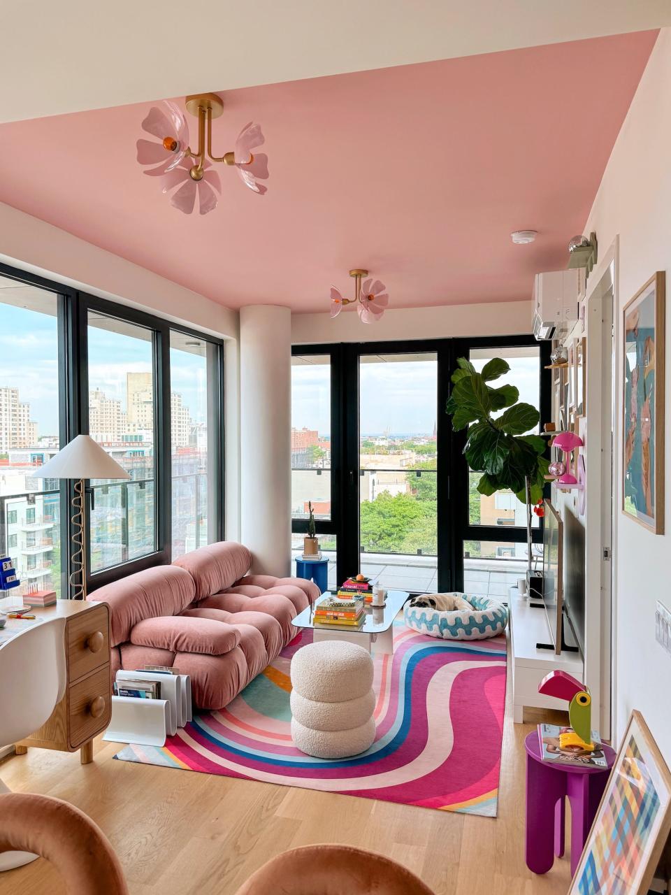 A living room with a pink ceiling, a multicolored rug, and a pink, rounded couch.