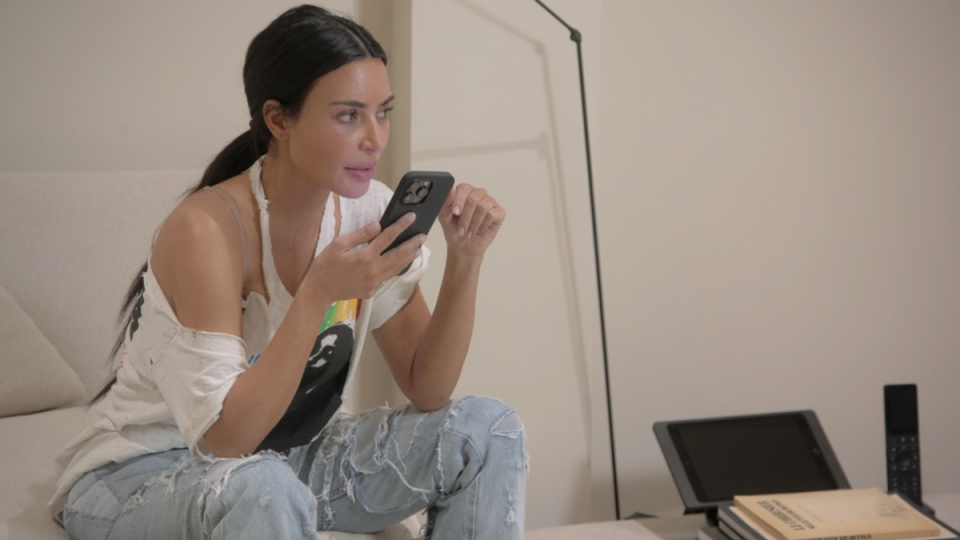 Person in a casual outfit sits on a sofa looking intently at a smartphone with a laptop nearby