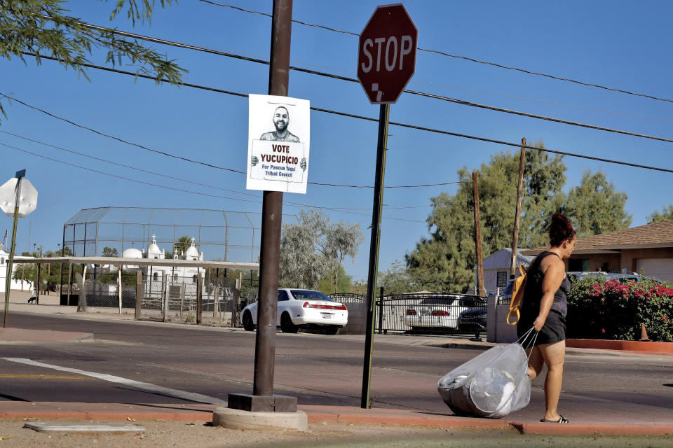 In this June 18, 2020, photo, a woman walks to a bus stop in Guadalupe, Ariz. As the coronavirus spreads deeper across America, it's ravaging through the homes and communities of Latinos from the suburbs of the nation's capital to the farm fields of Florida to the sprawling suburbs of Phoenix and countless communities in between. (AP Photo/Matt York)