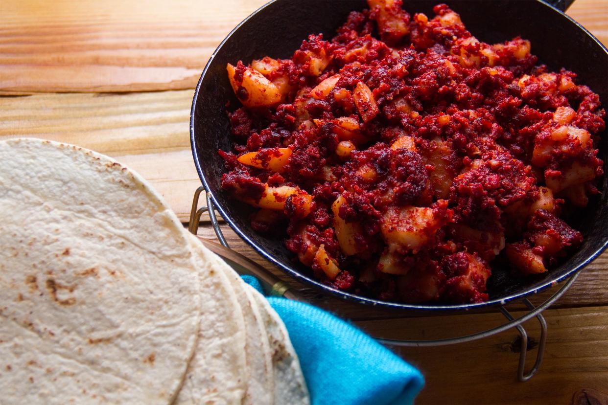 Potatoes with Mexican chorizo in a skillet with a side of flour tortillas on a wooden table