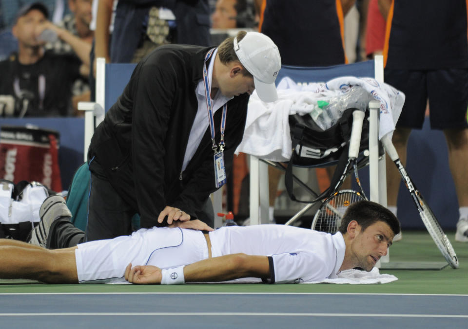 Novak Djokovic tumbado en el suelo mientras un médico le da un tratamiento en la espalda