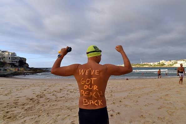 A man poses with a message on his back before enjoying his first swim after Bondi Beach reopened following a five week closure in Sydney.