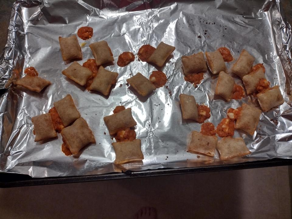 Baked rolls on a tray with some filling spilling out, next to a person's bare feet visible at the bottom