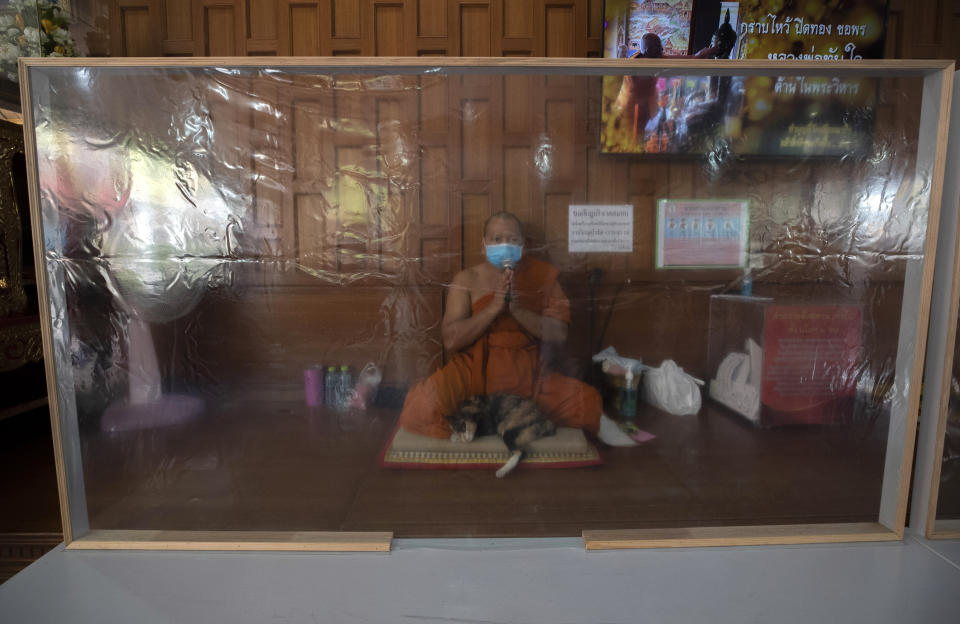 A Buddhist monk prays behind plastic sheets to help curb the spread of the coronavirus during the Thai New Year at the Samian Nari Temple Monday, April 13, 2020, in Bangkok, Thailand. The new coronavirus causes mild or moderate symptoms for most people, but for some, especially older adults and people with existing health problems, it can cause more severe illness or death. (AP Photo/Sakchai Lalit)