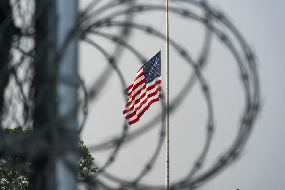 In this photo reviewed by U.S. military officials, a flag flies at half-staff in honor of the U.S. service members and other victims killed in the terrorist attack in Kabul, Afghanistan, as seen through a fence at Camp Justice, Sunday, Aug. 29, 2021, in Guantanamo Bay Naval Base, Cuba. Camp Justice is where the military commission proceedings are held for detainees charged with war crimes. (AP Photo/Alex Brandon)