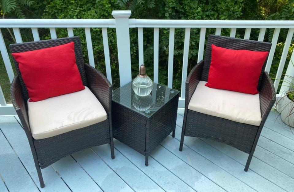 a reviewer photo of two rattan arm chairs with a matching side table with a glass top 