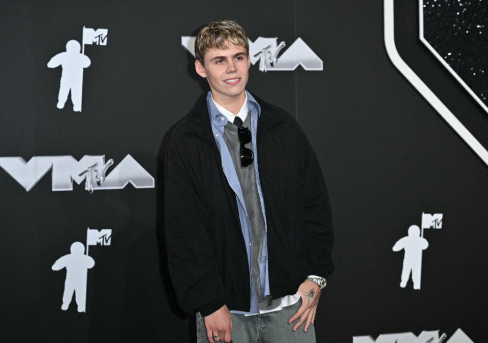 The Kid LAROI on the MTV VMA red carpet, wearing a jacket over a shirt and tie, posing with a hand in his pocket