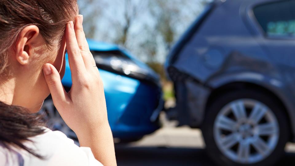 Stressed Driver Sitting At Roadside After Traffic Accident looking at the damage.