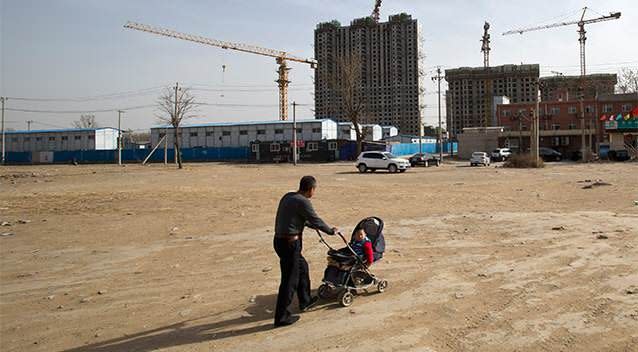 A man pushes a baby buggy near a construction site of a residential real estate project in a village on the outskirts of Beijing. Photo: AP.