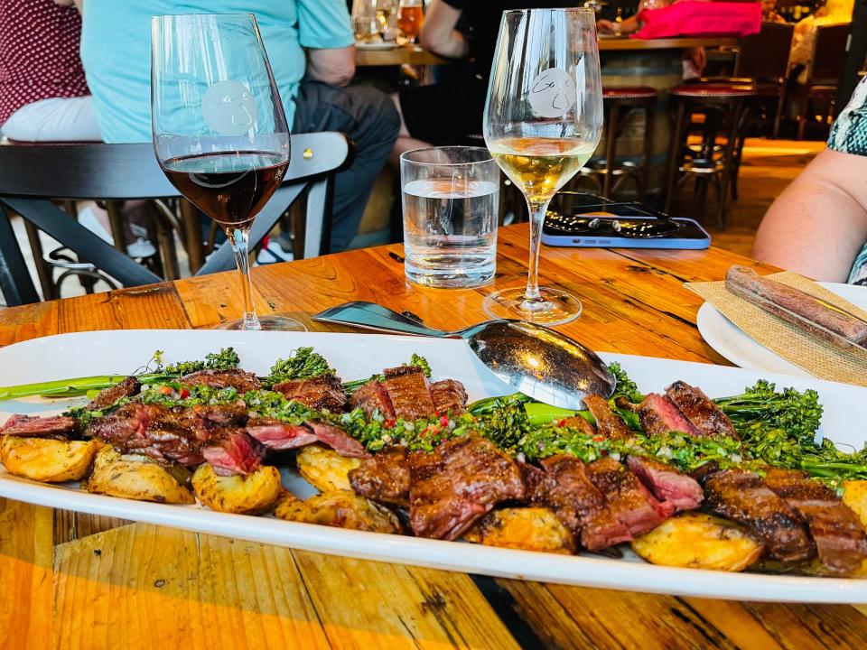 a platter of steak sitting in front of two glasses of wine at wine bar george in disney springs