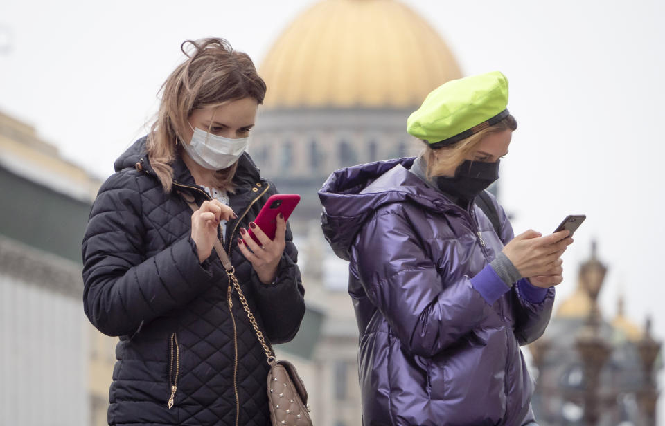 Women wearing face masks to protect against coronavirus look at their smartphones in downtown St.Petersburg, Russia, Monday, May 11, 2020. Russian President Vladimir Putin has declared an end to a nationwide partial economic shutdown but noted that some restrictions will remain. (AP Photo/Dmitri Lovetsky)