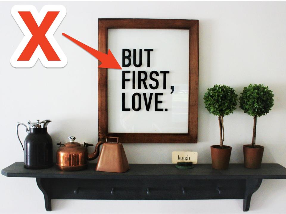 red x and arrow pointing to a "but first, love" sign on a shelf in a living room