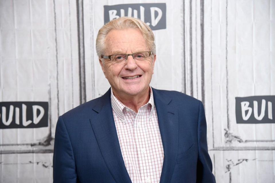 jerry springer at an event wearing a blue blazer and white and red checked shirt