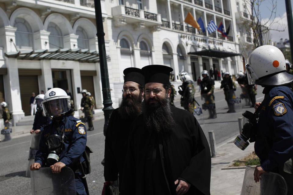 Greek Orthodox priests walk among riot police officers guarding a demonstration, in Athens on Wednesday, April 9, 2014. Greek unions launched an anti-austerity general strike on Wednesday that halted train and island ferry services while disrupting state hospitals and other public services. (AP Photo/Kostas Tsironis)